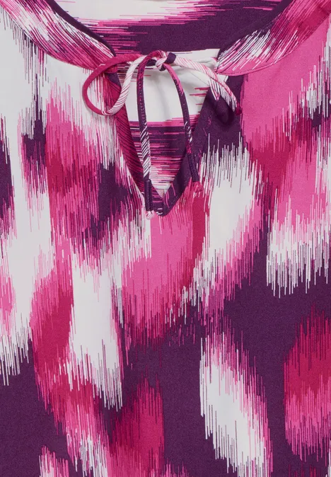 Bunte Bluse mit pink-weißem Muster und Schleife am Ausschnitt.